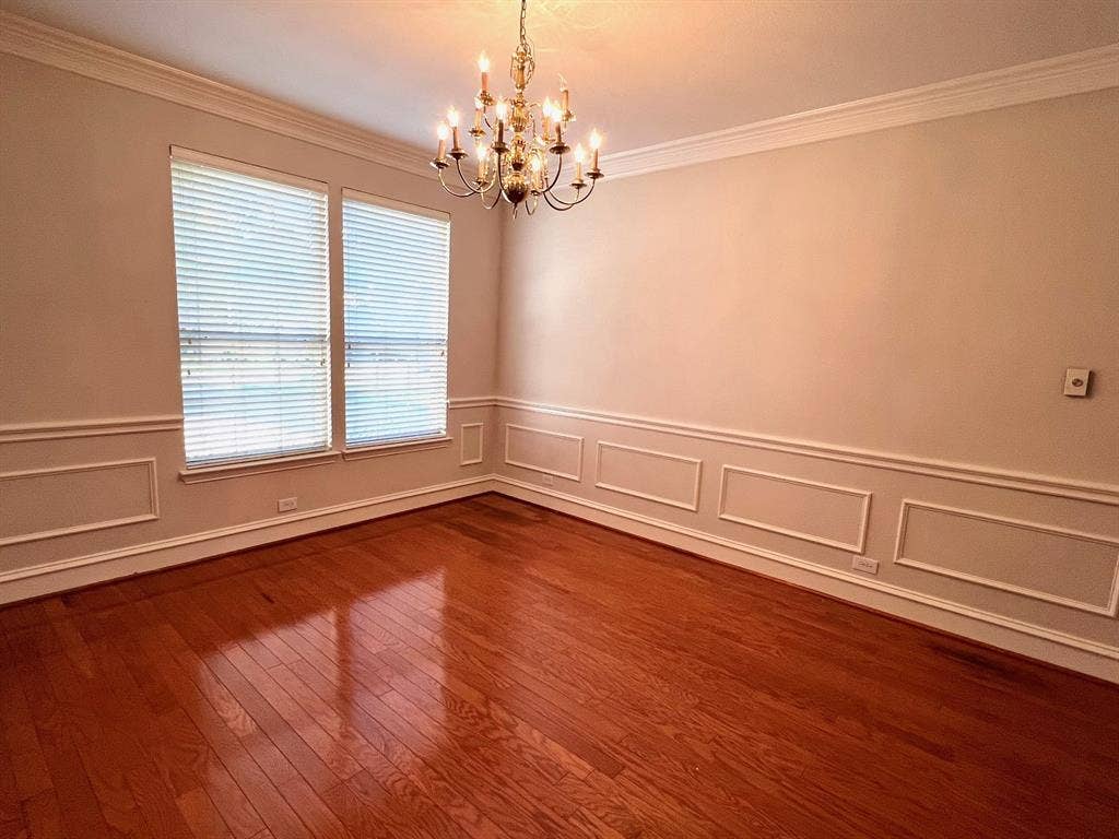 Room featuring wood-finish flooring, wainscoting, crown molding, and a multi-tiered metal chandelier