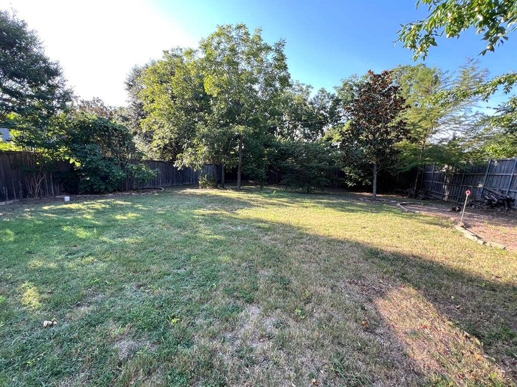 Backyard featuring a grass lawn, mature trees, wood privacy fencing, and stone-bordered landscaping beds