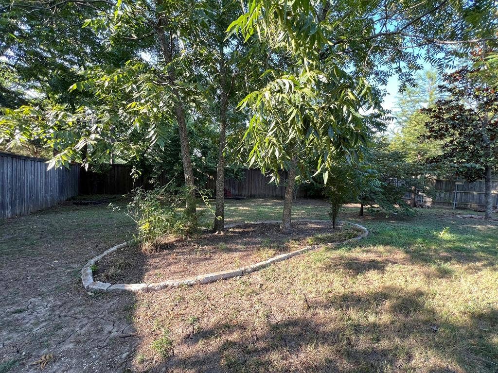 Backyard space featuring mature trees, stone-edged landscaping borders, and full perimeter wood fencing