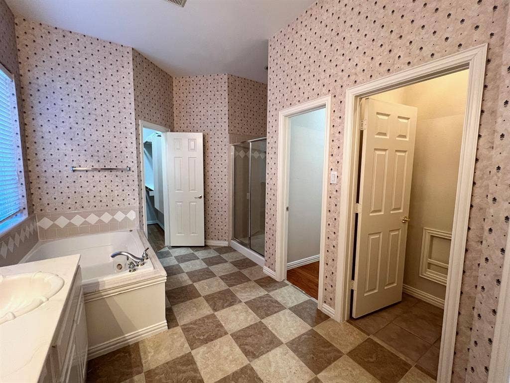Soaking tub with tile surround, glass-enclosed shower, dual interior doors, and checkerboard-patterned flooring