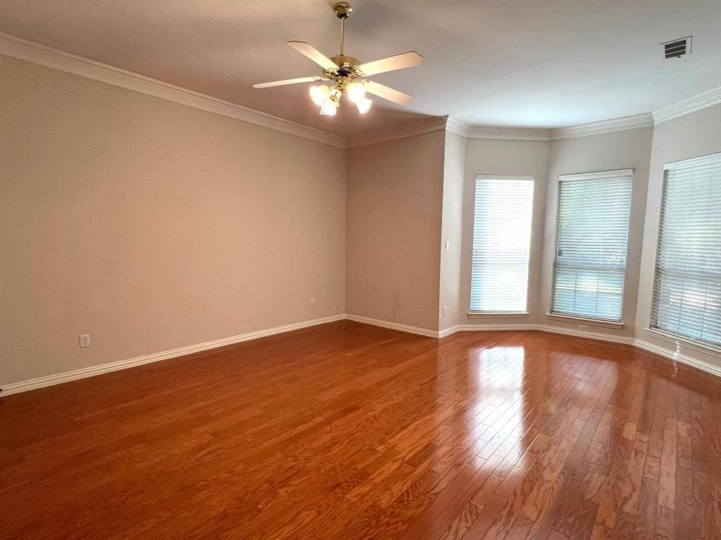 Living space featuring wood-finish flooring, crown molding, a central ceiling fan with multi-light fixture, and a bay window configuration