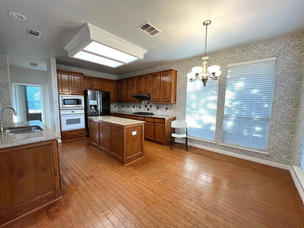 Kitchen featuring wood-finish cabinetry, stone-surfaced countertops, a center island, wood-finish flooring, and a decorative chandelier