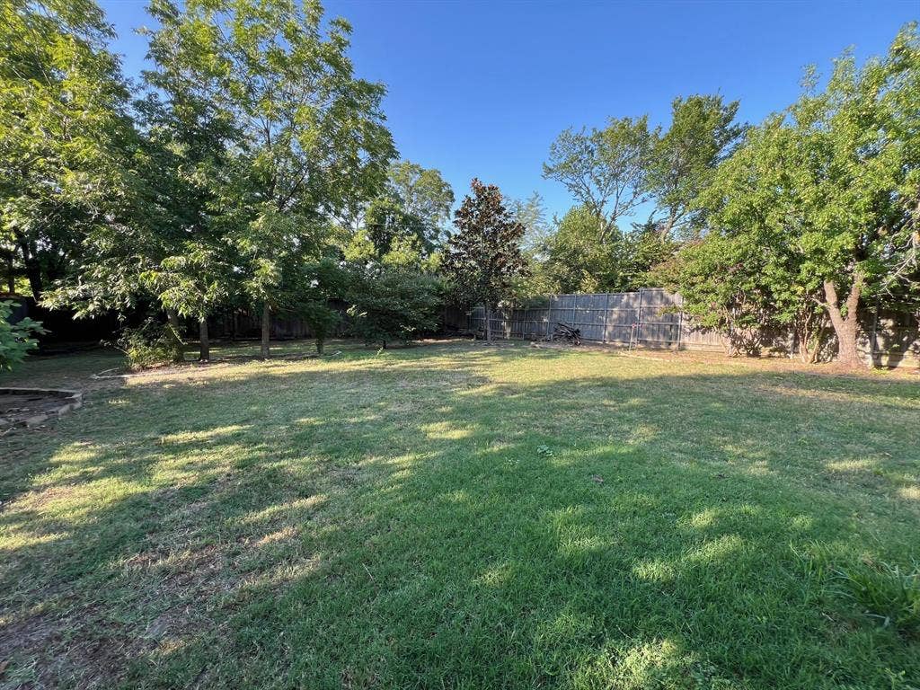 Expansive backyard featuring a large grass lawn, mature trees, and wooden perimeter fencing