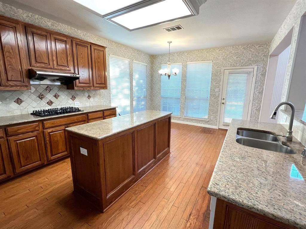 Kitchen featuring wood cabinetry, stone-surface countertops, central island, dual-basin sink with pull-down faucet, and wood-finish flooring