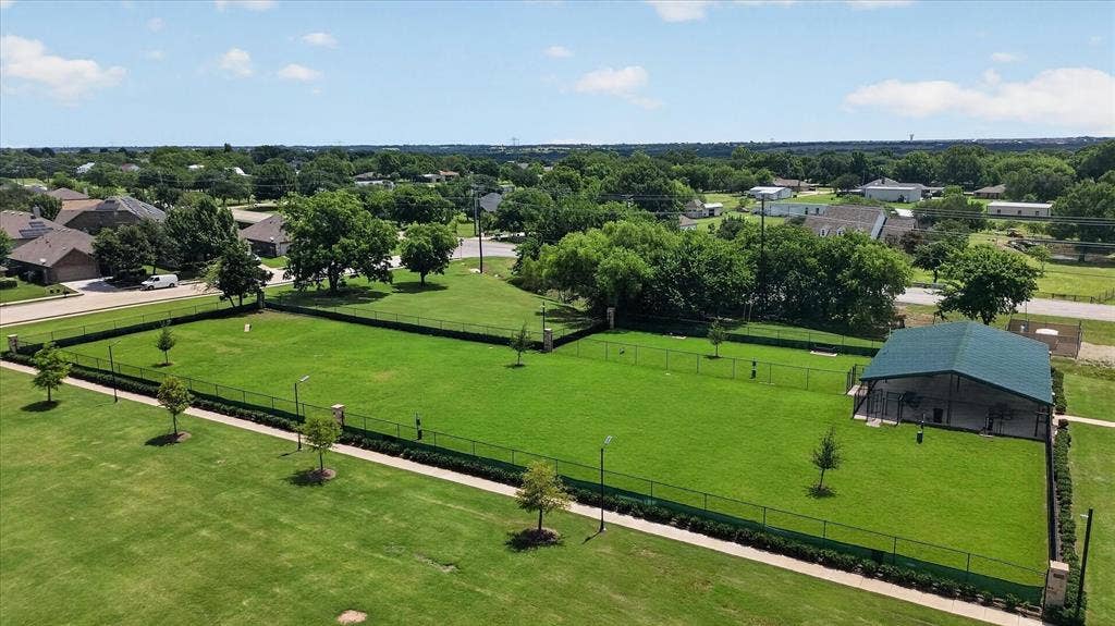 Expansive fenced grass area featuring a covered pavilion, mature trees, and perimeter landscape hedging