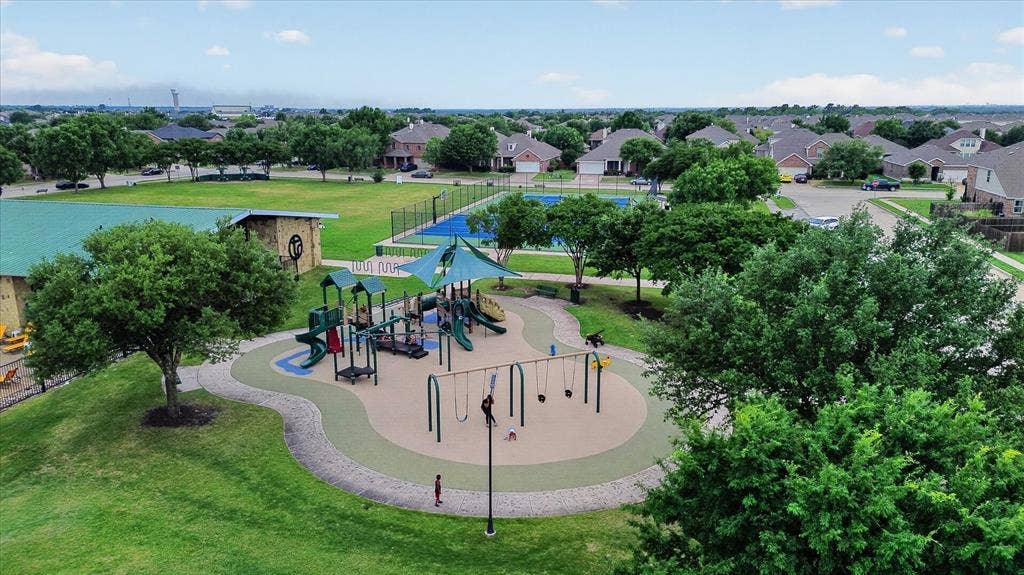 Community recreational area featuring a playground with shade structures, a fenced tennis court, and expansive green space