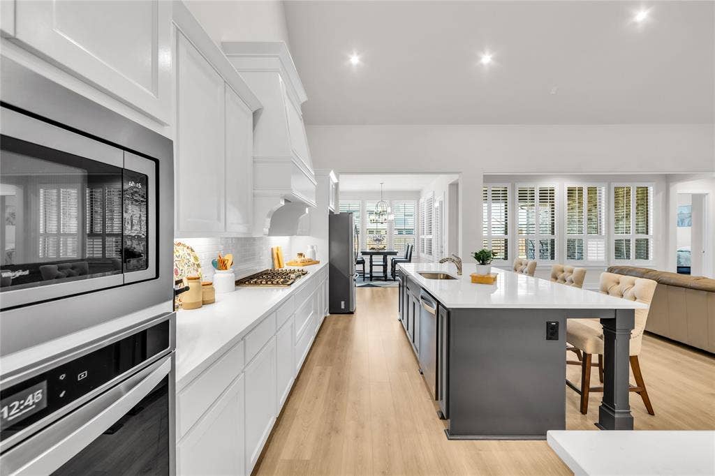 2971 Gaulding Drive, Prosper, TX 75078 Kitchen featuring white shaker-style cabinetry, quartz countertops, a central island with a contrasting base, wood-finish flooring, and stainless-steel built-in appliances