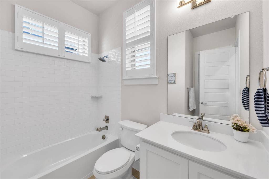 2971 Gaulding Drive, Prosper, TX 75078 Bathroom featuring white cabinetry with a solid surface countertop, an undermount oval sink, shower-tub combination with white subway tile surround, plantation shutters, and a large wall-mounted mirror