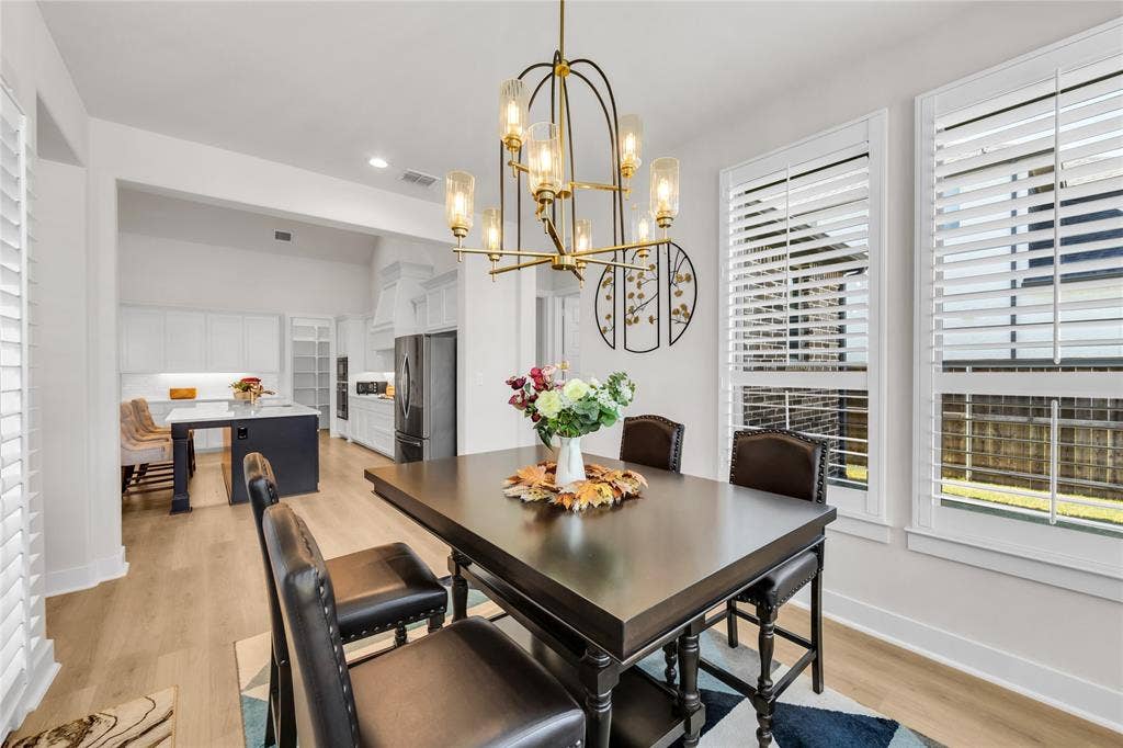 2971 Gaulding Drive, Prosper, TX 75078 Dining area featuring a multi-light metal chandelier, wood-finish flooring, and white plantation shutters