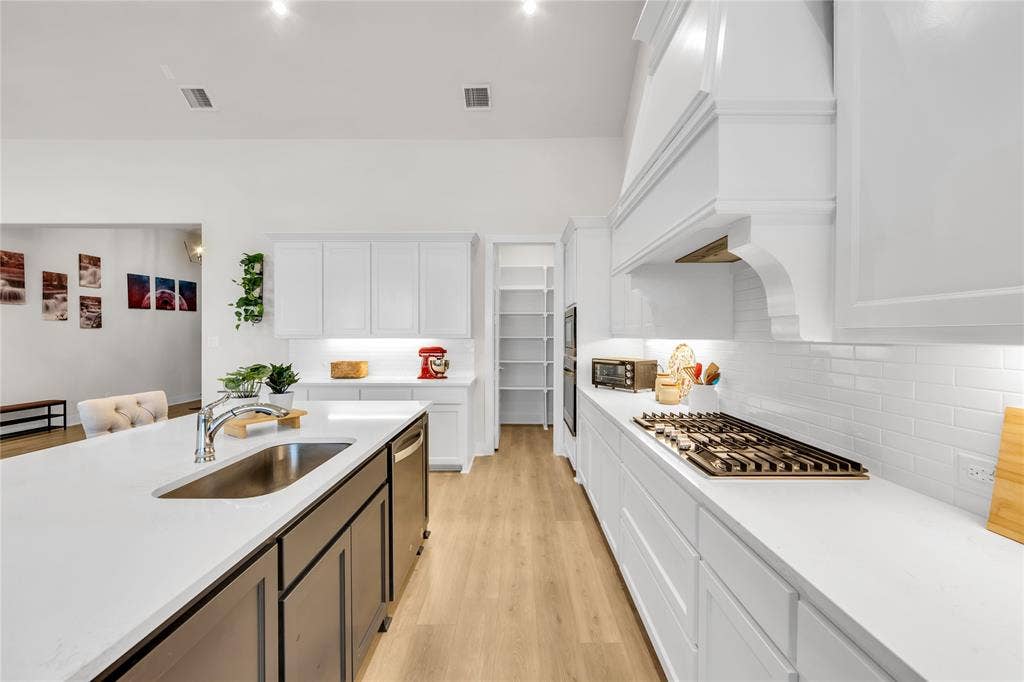 2971 Gaulding Drive, Prosper, TX 75078 Kitchen featuring an island with a stainless steel undermount sink, white cabinetry, a built-in range hood, a tiled backsplash, and wood-finish flooring