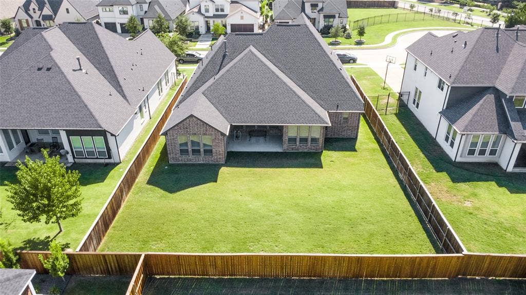 2971 Gaulding Drive, Prosper, TX 75078 Aerial perspective of a multi-gabled brick residence featuring a covered patio and a fully enclosed wood-fenced rear yard with a grass lawn
