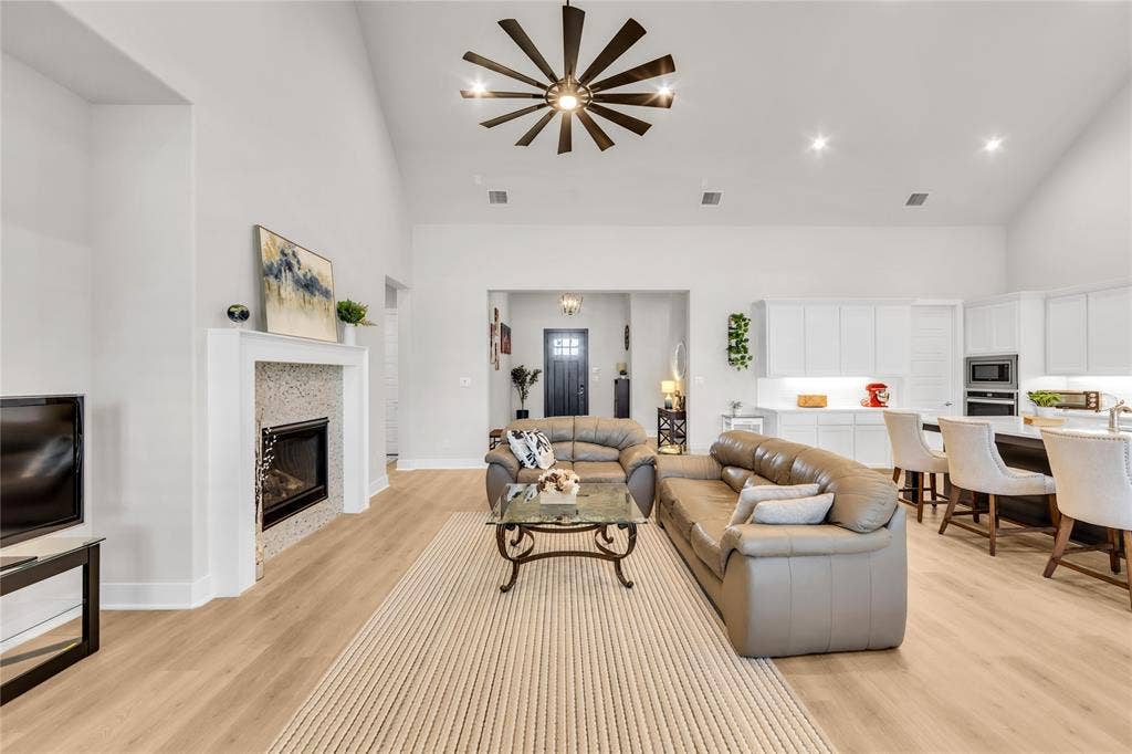 2971 Gaulding Drive, Prosper, TX 75078 Vaulted ceiling featuring a central multi-blade light fixture, wood-finish flooring, stone-tiled fireplace, and kitchen with white cabinetry and a center island