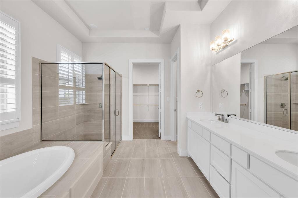 2971 Gaulding Drive, Prosper, TX 75078 Dual-sink vanity with white cabinetry and solid-surface countertops, walk-in tile shower, separate soaking tub, and walk-in closet with built-in shelving