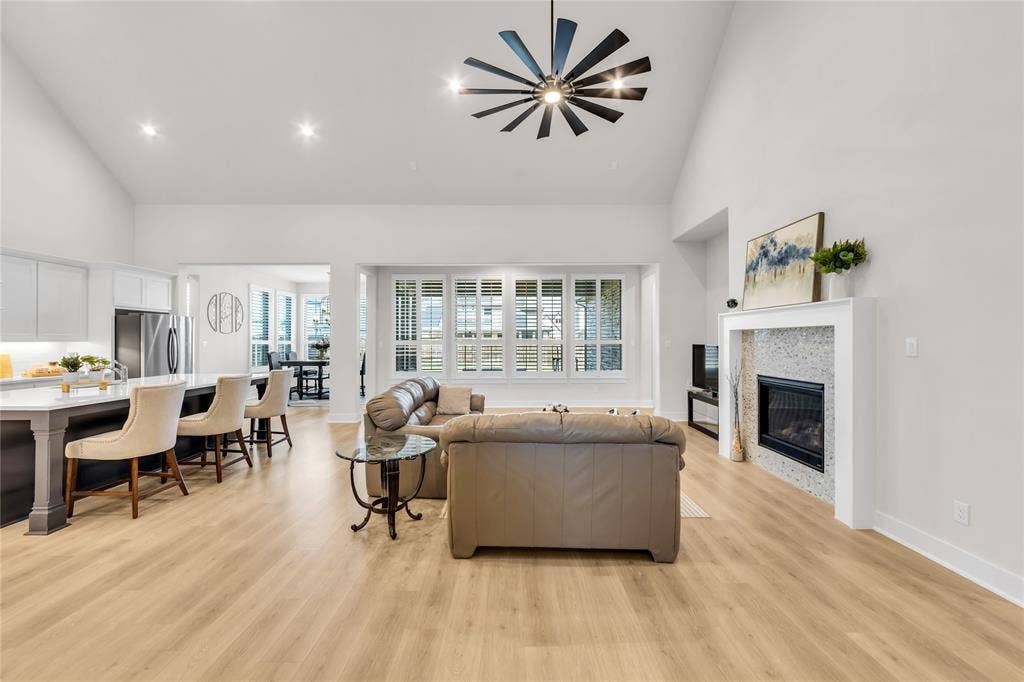 2971 Gaulding Drive, Prosper, TX 75078 Open-concept interior featuring vaulted ceilings, wood-finish flooring, a contemporary ceiling fan, and a fireplace with a decorative stone surround