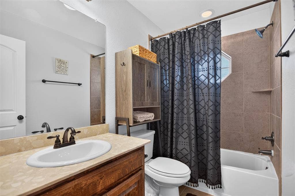 122 Anns Way, Forney, TX 75126 Bathroom featuring a wood-finish vanity with a stone-composite countertop, integrated oval basin, and oil-rubbed bronze hardware, complemented by a tiled shower surround and a fixed octagonal window