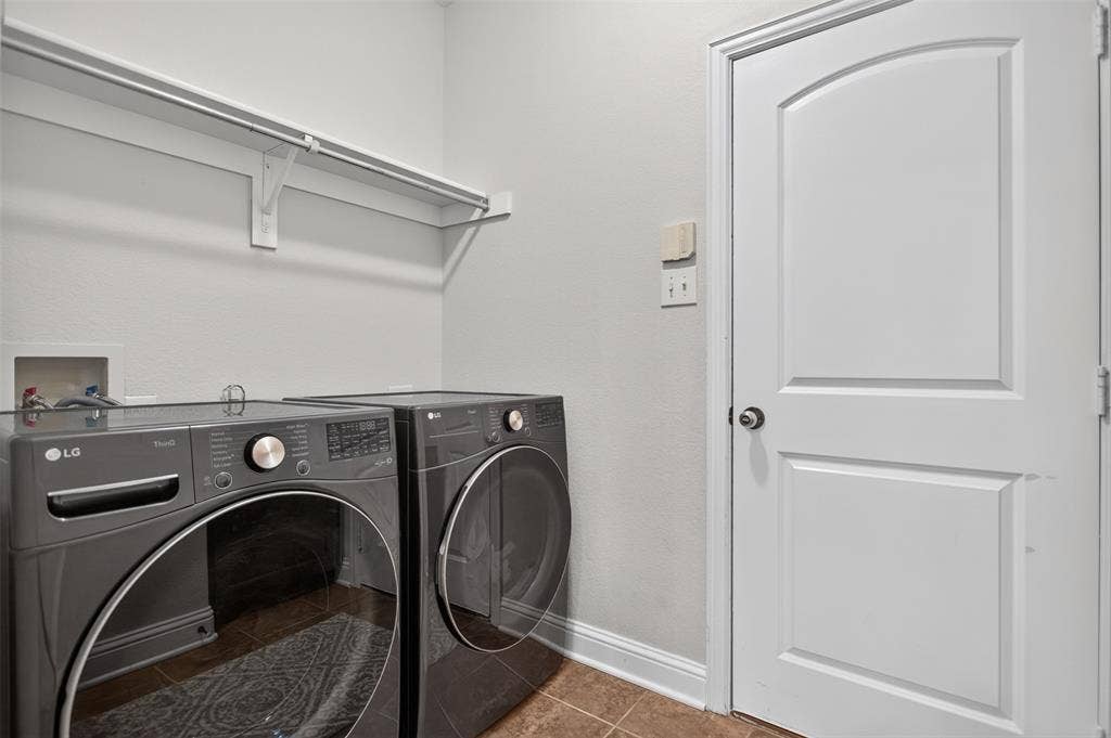 122 Anns Way, Forney, TX 75126 Laundry room featuring a single-panel arched interior door, installed wall-mounted shelving with integrated hanging rod, ceramic tile flooring, and recessed laundry hookups