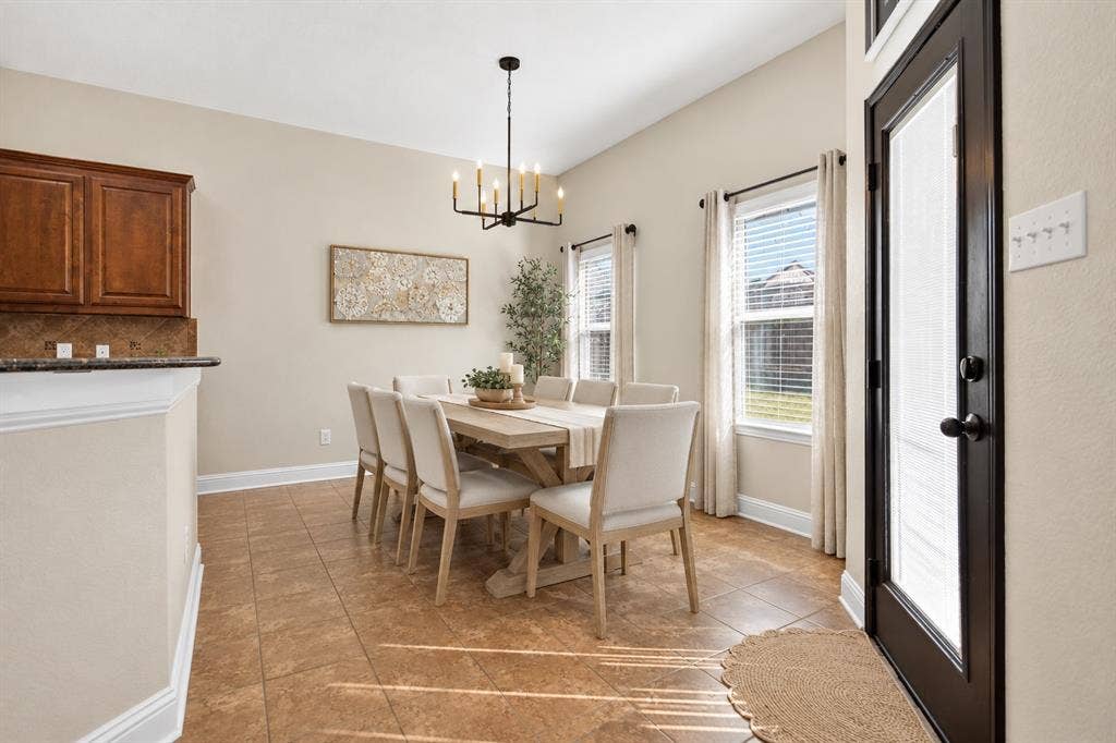 122 Anns Way, Forney, TX 75126 Dining area featuring ceramic tile flooring, a multi-light metal chandelier, and windows with neutral-tone treatments, accented by a door with dark trim