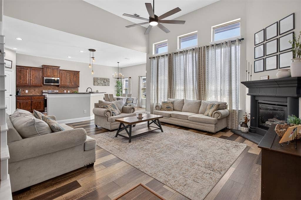 122 Anns Way, Forney, TX 75126 Vaulted ceiling with a multi-blade ceiling fan, expansive windows, dark-finish fireplace surround, and wood-finish flooring