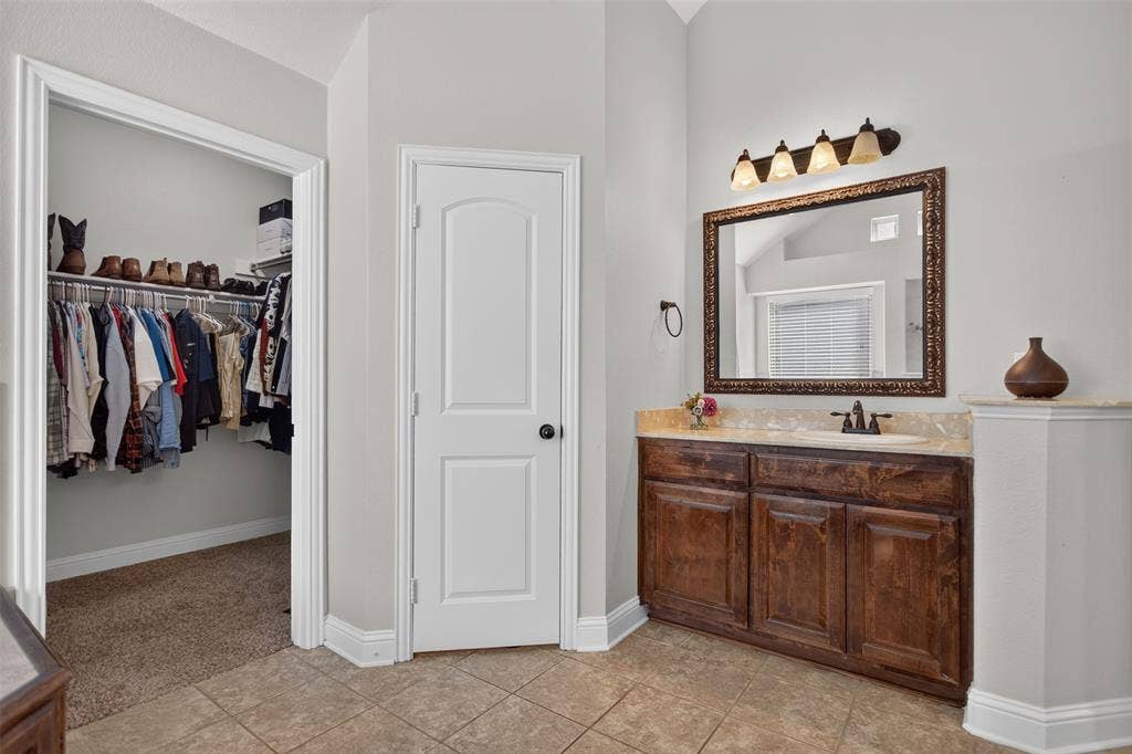 122 Anns Way, Forney, TX 75126 Vanity featuring stained wood cabinetry, stone-finish countertop, undermount sink, and wall-mounted light fixture
