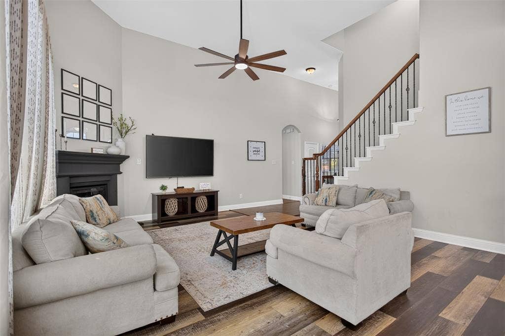 122 Anns Way, Forney, TX 75126 Vaulted ceiling with an integrated multi-blade ceiling fan, dark wood-finish flooring, fireplace with a painted mantel, and a staircase featuring metal balusters