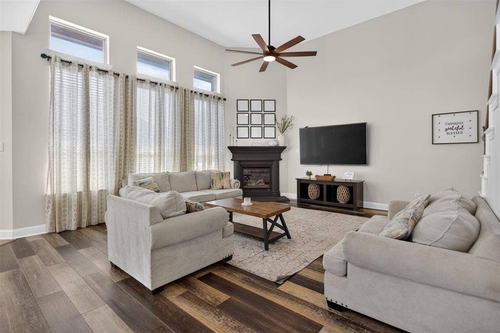 122 Anns Way, Forney, TX 75126 Living area featuring high ceilings, wood-finish flooring, transom windows, and a dark-toned fireplace surround with a ceiling fan