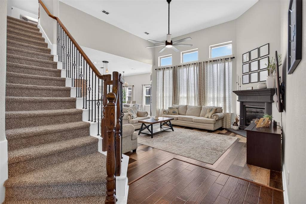 122 Anns Way, Forney, TX 75126 High-ceiling living area featuring wood-finish flooring, a dark-toned fireplace mantel, a multi-pane window configuration, and a staircase with wrought iron spindles and a stained wood banister