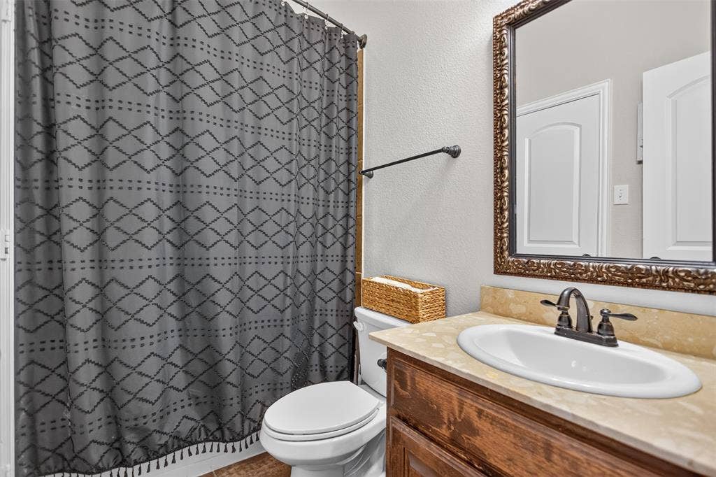 122 Anns Way, Forney, TX 75126 Bathroom vanity featuring a natural stone countertop, an integrated drop-in sink, a metal dual-handle faucet, and an ornate framed wall mirror