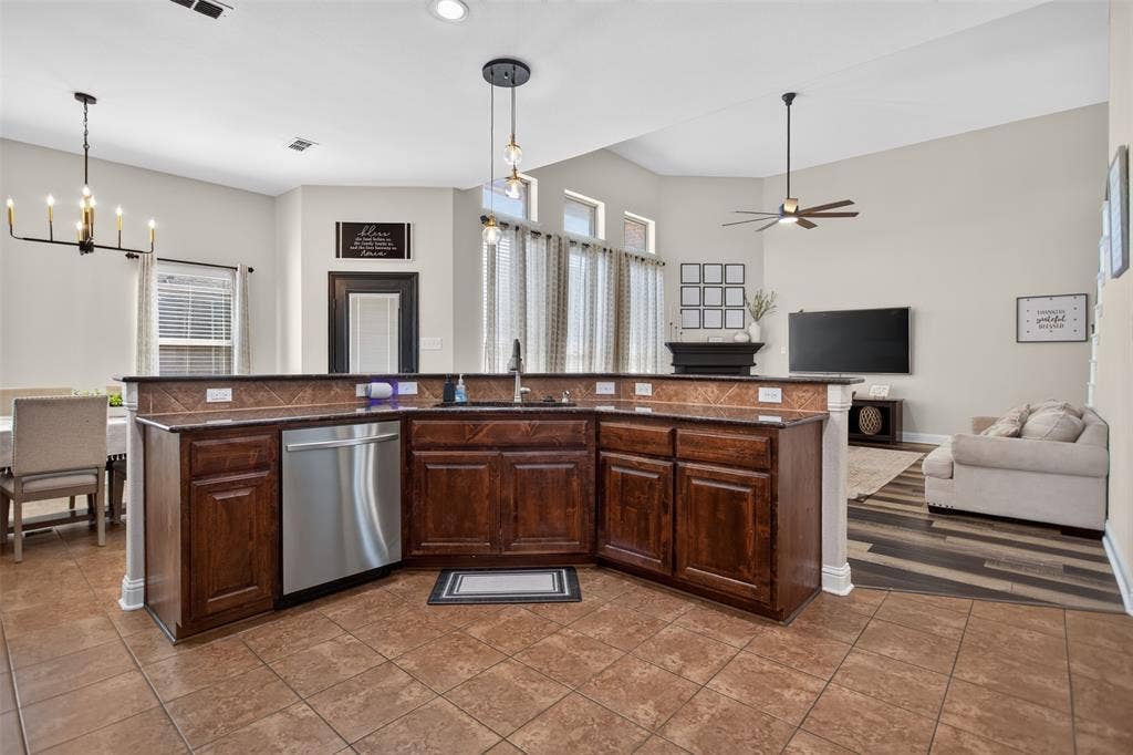 122 Anns Way, Forney, TX 75126 Kitchen featuring dark-toned wooden cabinetry, dark stone countertops, stainless steel dishwasher, tile flooring, and vaulted ceilings with pendant lighting