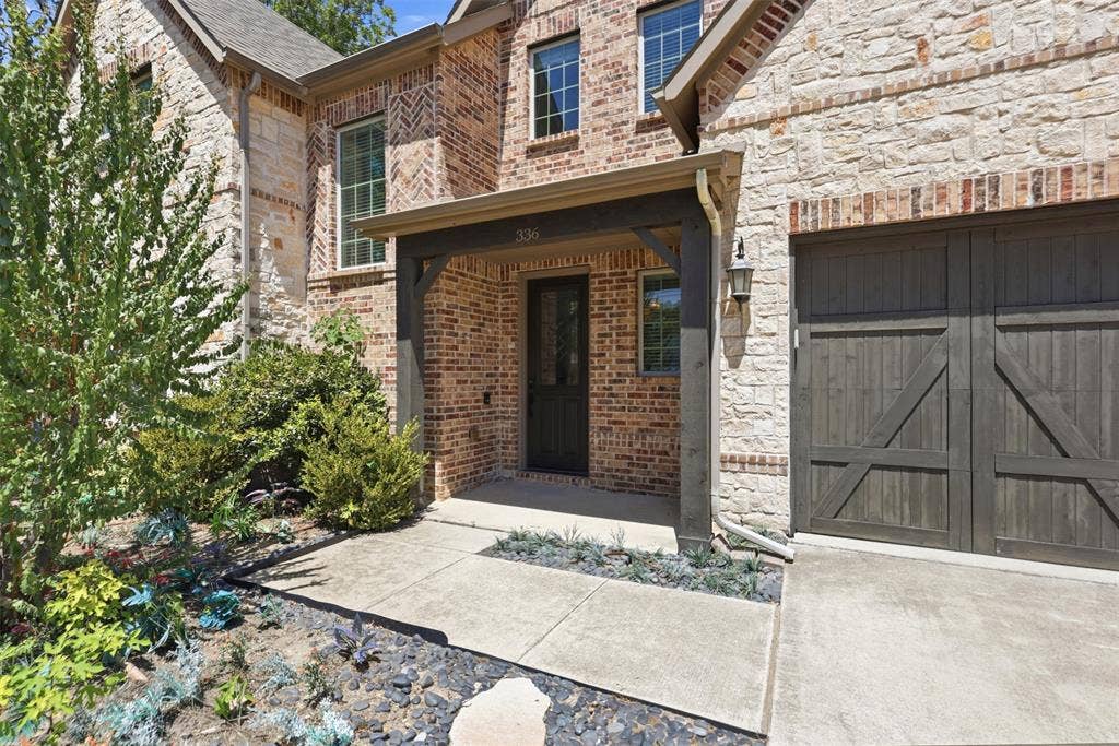 336 Kaye Street, Coppell, TX 75019 Exterior facade featuring masonry stone and brick veneer, covered entryway, wood-finish garage door, and metal-framed windows