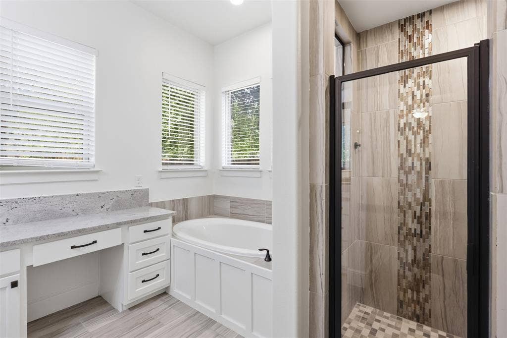 336 Kaye Street, Coppell, TX 75019 Bathroom featuring a built-in vanity with light-toned stone countertop, soaking tub with paneled surround, walk-in shower with decorative mosaic tile accent, and tile flooring