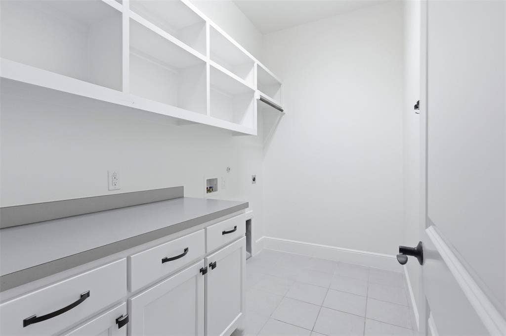 336 Kaye Street, Coppell, TX 75019 Utility room featuring white shaker-style cabinetry, matte black hardware, grey solid-surface countertops, open wall shelving, and neutral floor tile