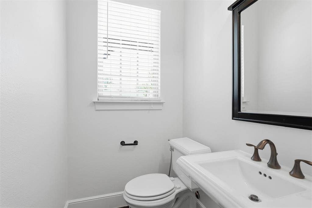 336 Kaye Street, Coppell, TX 75019 Bathroom featuring a white pedestal sink, oil-rubbed bronze widespread faucet, framed wall mirror, and horizontal slat window blinds