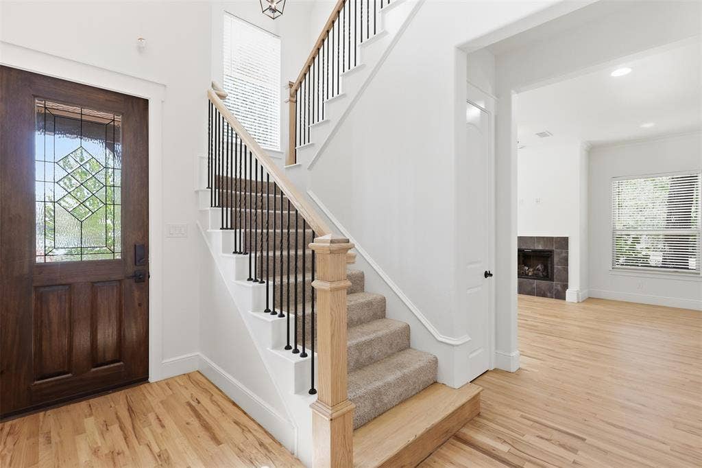 336 Kaye Street, Coppell, TX 75019 Stained wood entry door with decorative glass inlay, wood-finish flooring, staircase featuring a natural wood handrail and black metal balusters, and a fireplace with tile surround