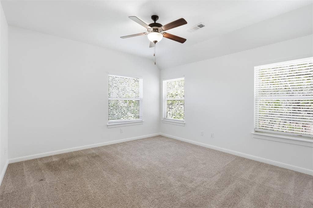 336 Kaye Street, Coppell, TX 75019 Neutral carpeted flooring, vaulted ceiling, and three windows featuring blinds, centered by a ceiling fan with integrated lighting