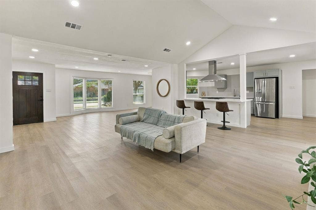 Open-concept interior featuring vaulted ceilings, wood-finish flooring, recessed lighting, a bay window, and a kitchen peninsula with a stainless-steel range hood