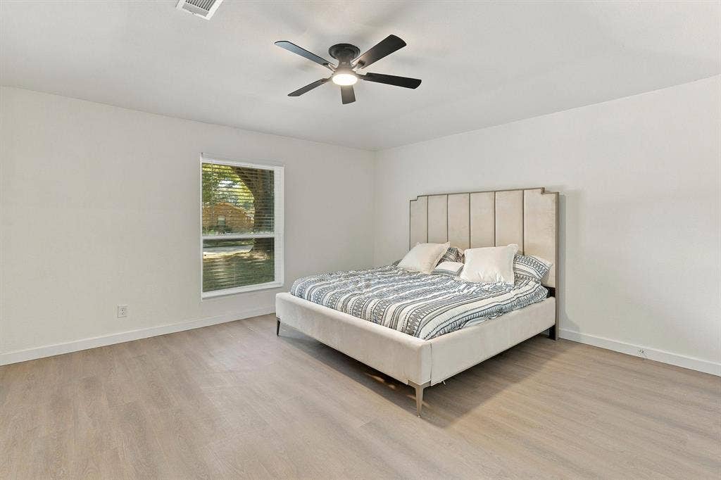 Neutral-toned wood-finish flooring, ceiling fan with integrated lighting, and a single-pane window