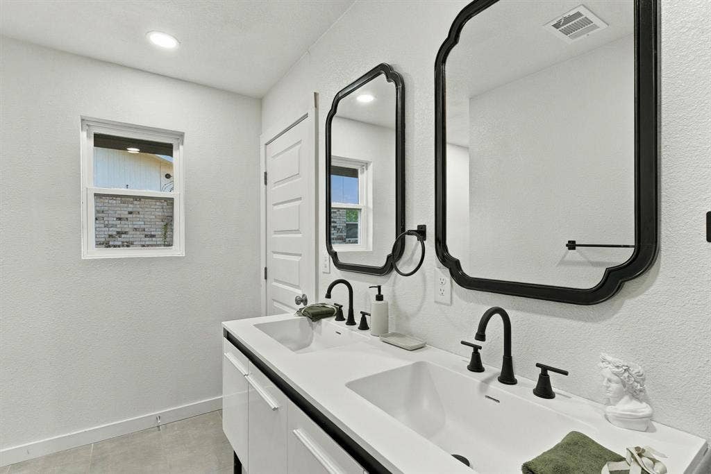 Dual-sink vanity featuring a solid-surface countertop, matte black widespread faucets, scalloped-edge mirrors, and white cabinetry