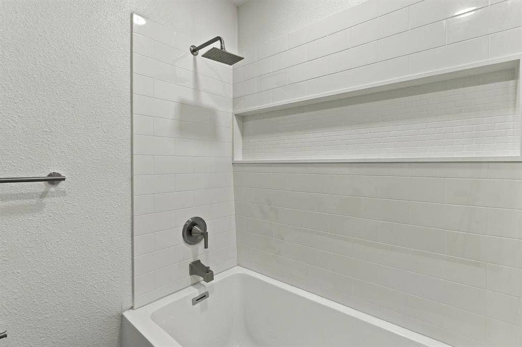 Shower area featuring white subway tile surround, built-in recessed storage niche, rectangular rainfall shower head, and metallic finish plumbing fixtures