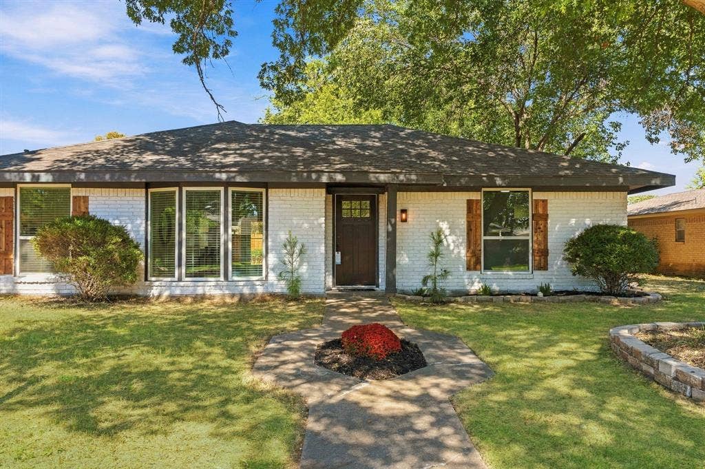 Painted brick exterior featuring a multi-pane front door, shutter-style window accents, a low-pitched roofline, and a stone-bordered front garden bed