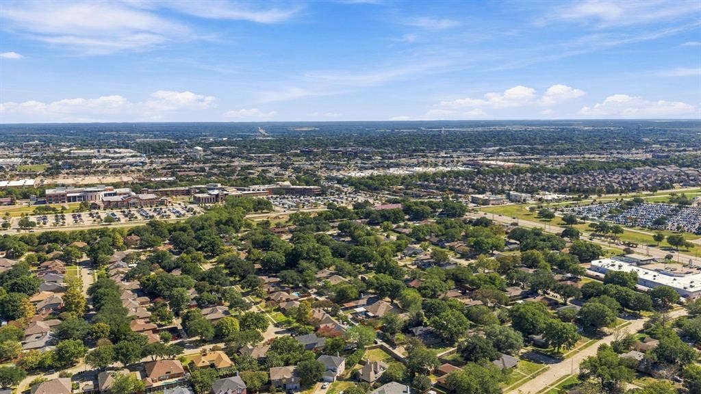 Aerial perspective of the residential area featuring mature tree canopy, dense landscaping, established road infrastructure, and expansive horizon