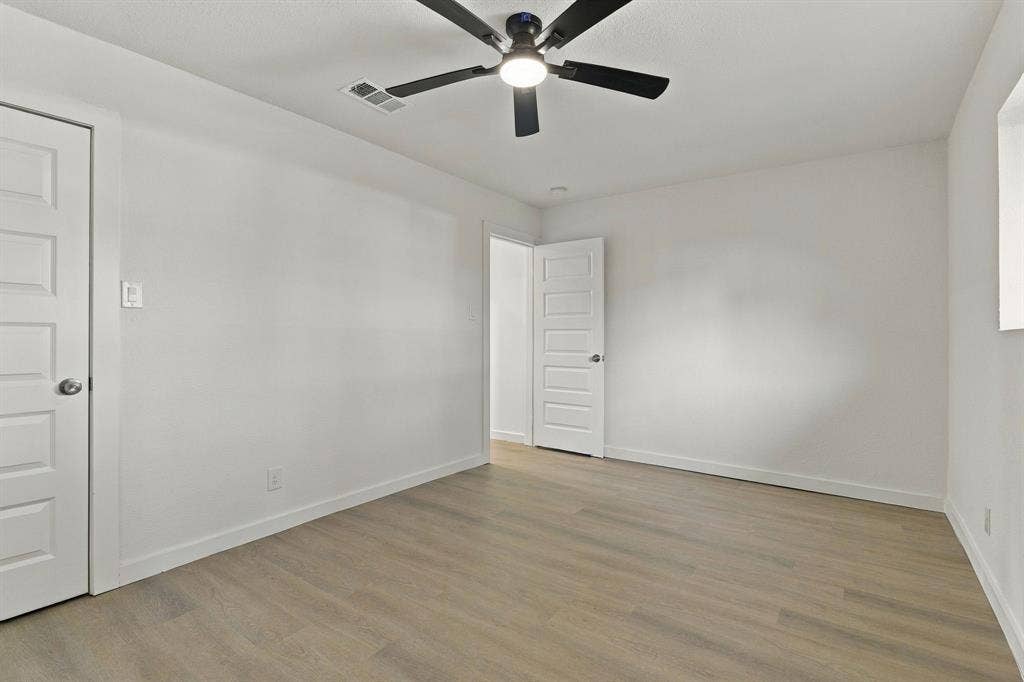 Neutral-toned wood-finish flooring, five-panel interior doors, and a ceiling fan with integrated lighting