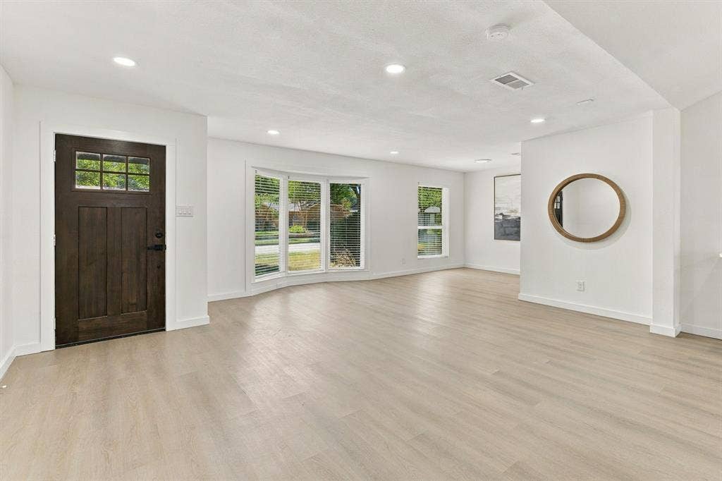 Open-concept interior featuring light-toned wood-finish flooring, recessed lighting, a bay window, and a dark-stained wood entry door with glass pane detailing