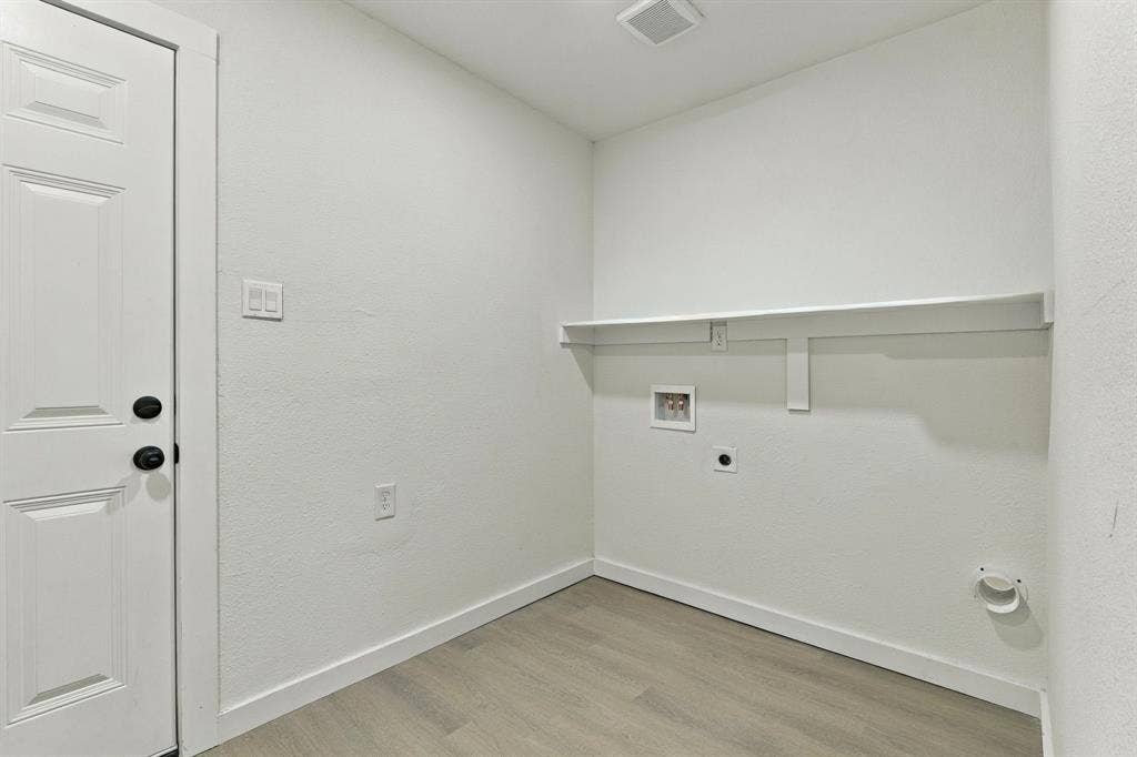 Laundry area featuring wood-finish flooring, a wall-mounted shelving unit, and dedicated utility connections