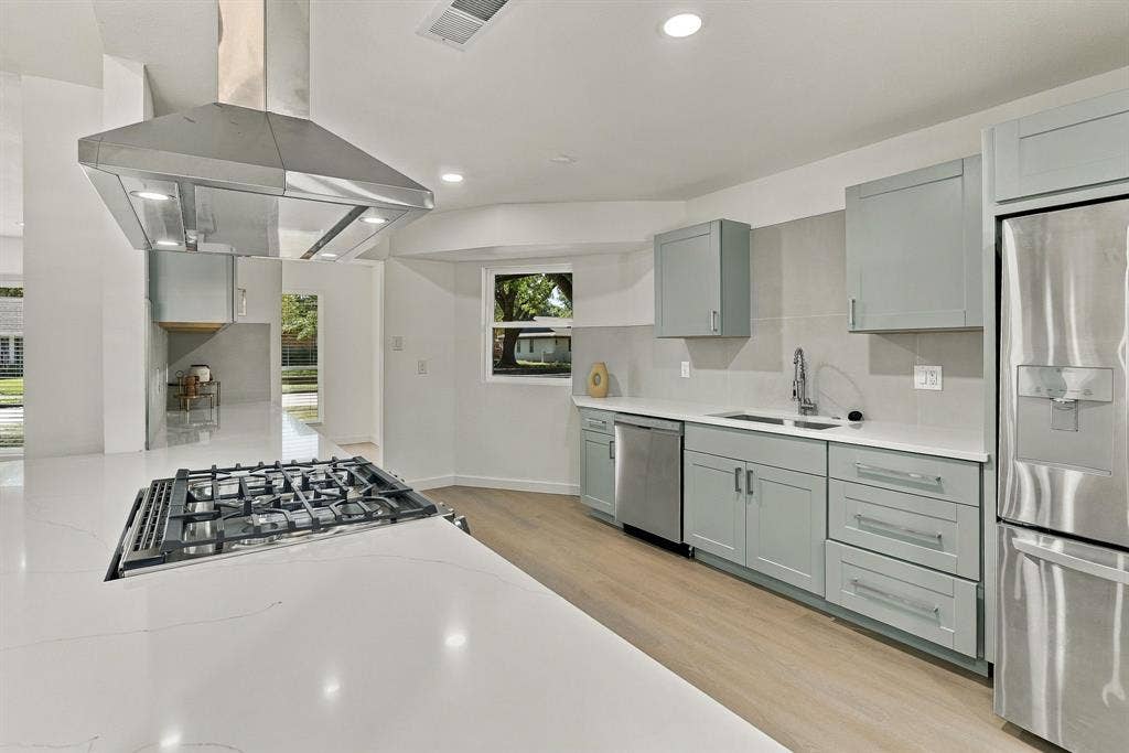 Kitchen featuring light-toned cabinetry, quartz countertops, stainless steel appliances including a gas cooktop with an overhead range hood, and wood-finish flooring