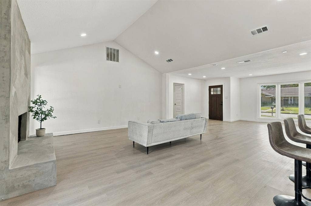 Vaulted ceiling, stone-surround fireplace, wood-finish flooring, recessed lighting, and large windows