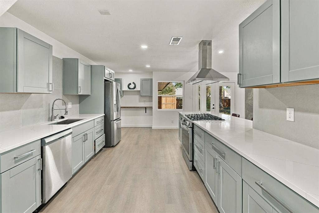 Kitchen featuring stainless steel appliances, light-toned shaker cabinetry, stone-surface countertops, a stainless steel range hood, and wood-finish flooring