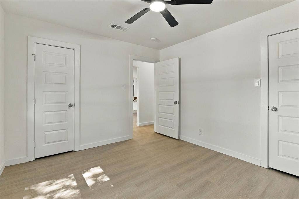 Neutral-toned wood-finish flooring, crisp white walls, and matte black ceiling-mounted light fixture with a five-blade fan