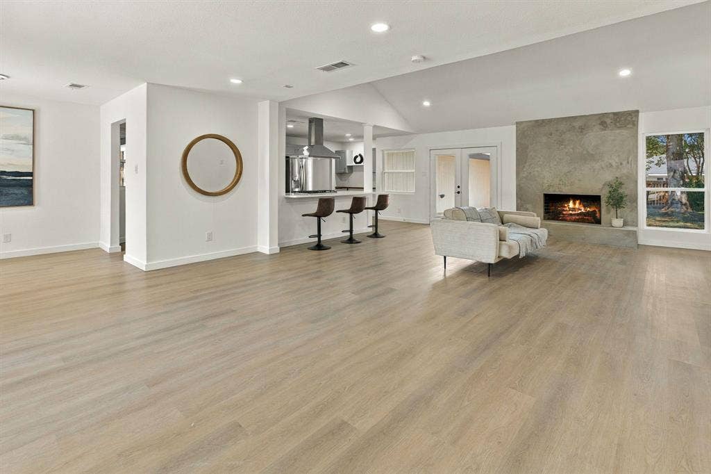 Open-concept floor plan featuring wood-finish flooring, vaulted ceilings, full-height masonry fireplace, and kitchen peninsula with bar-top seating