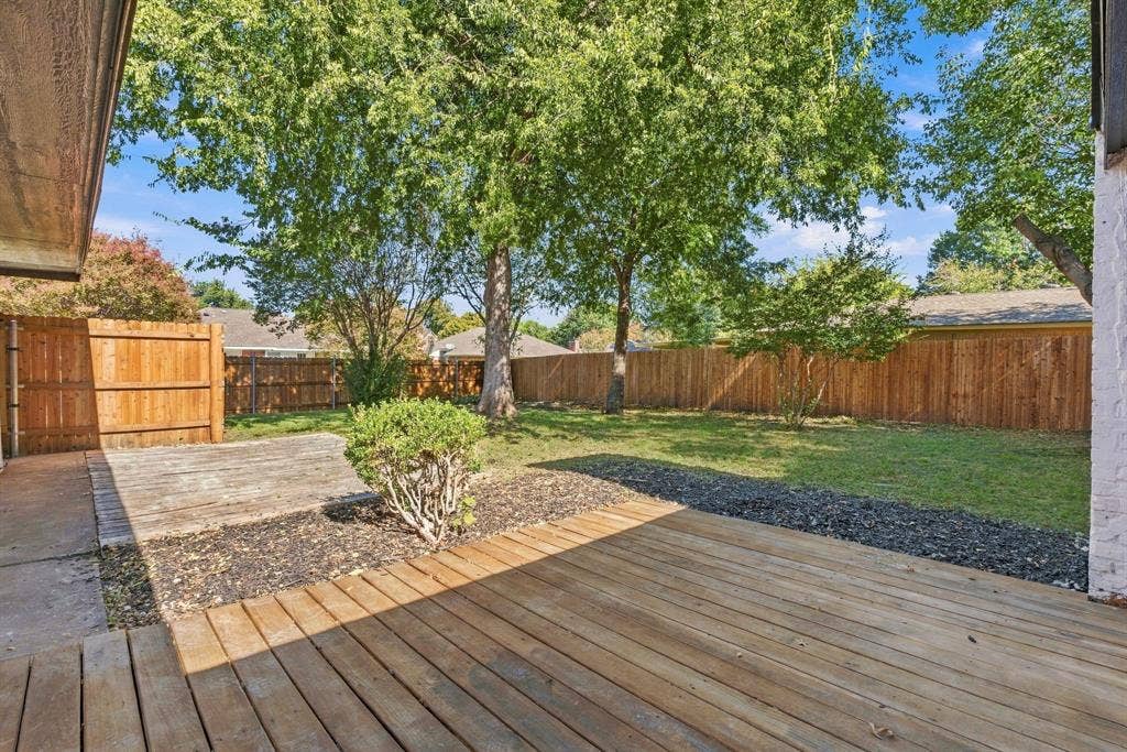 Backyard featuring a wood deck, concrete patio, perimeter wood fencing, and mature trees