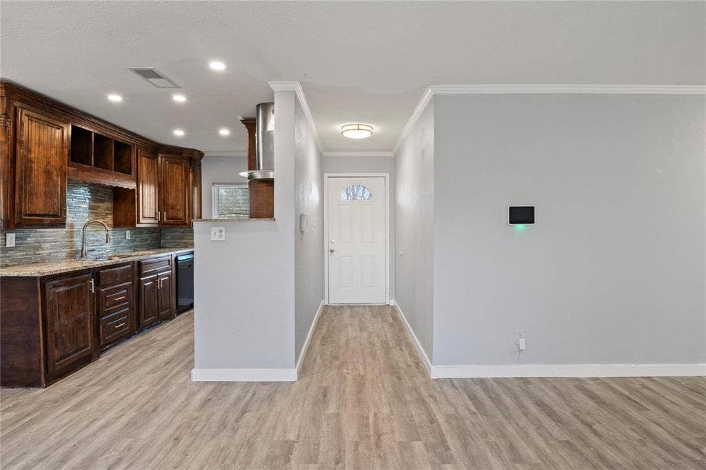 6543 Gentle River, Dallas, TX 75241 Kitchen featuring wood-finish cabinetry, stone-texture backsplash, and stone-look countertops, accompanied by wood-finish flooring and a single-light entry door